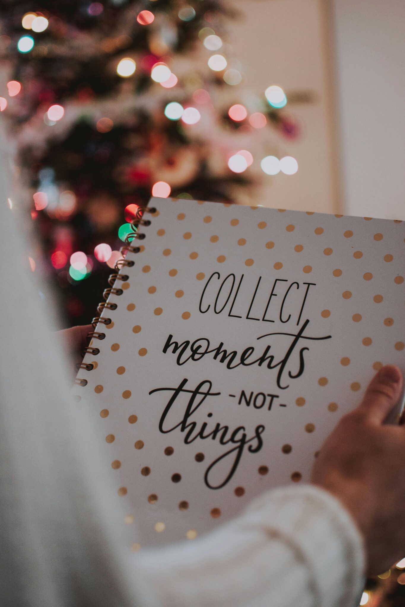 A hand holding a notebook with 'Collect moments not things' during a festive Christmas season.